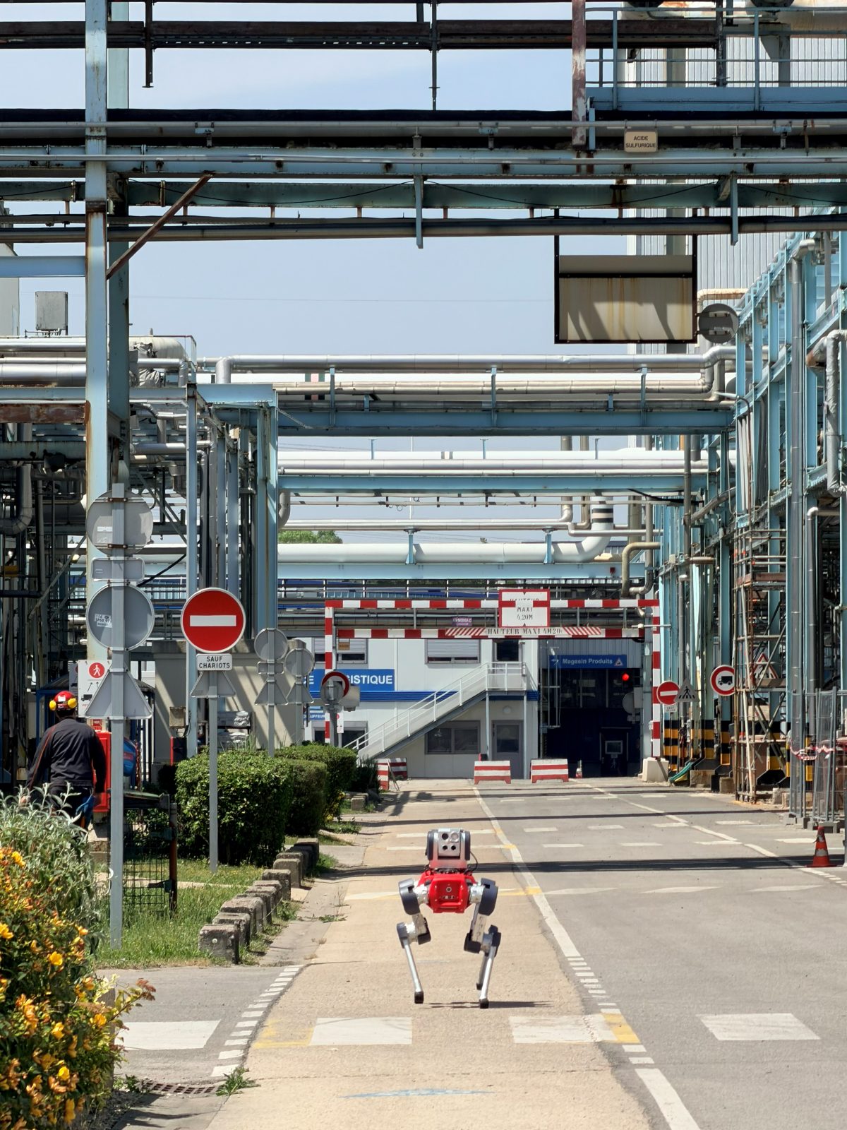 A quadruped inspection robot on an autonomous round through an industrial plant, between pipe racks.